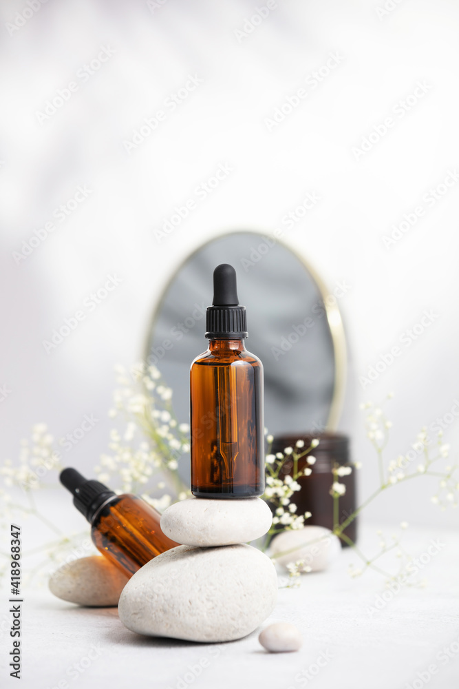Fototapeta premium Bottle of dark amber glass with essential oil on stack of natural stones, candle and mirror
