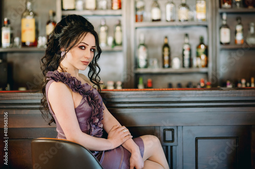 Luxury girl sitting and posing for camera in pub in front of bar with tasty cocktails