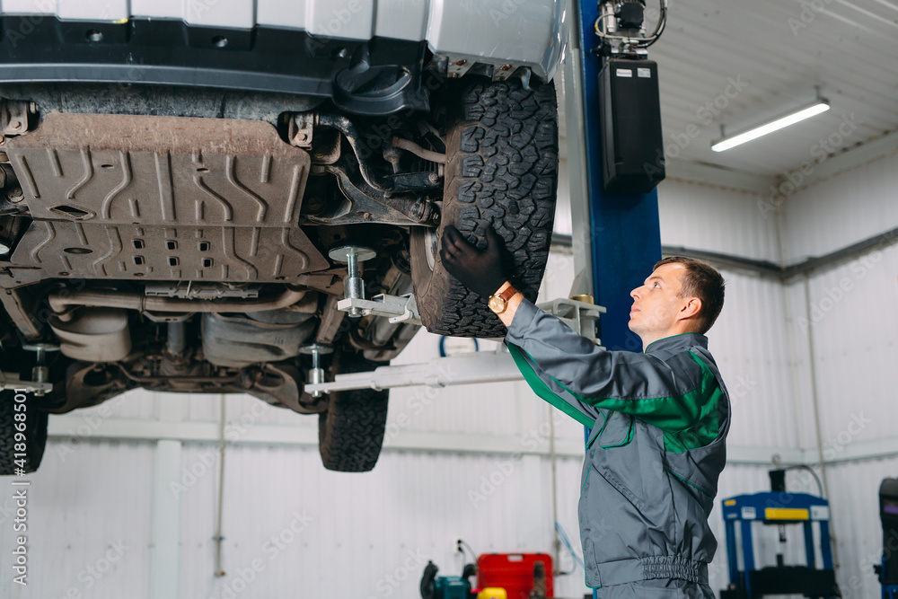 Car lifted in automobile service for fixing, worker repairs the wheel,