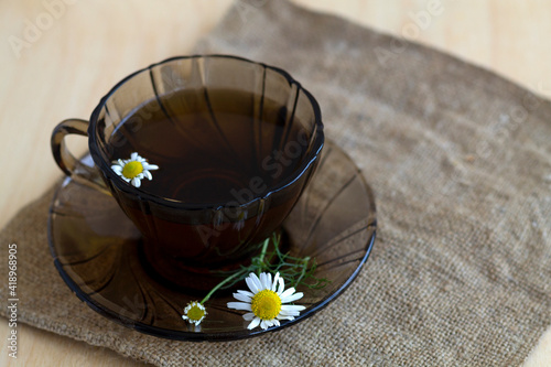 cup of tea with flowers.hot glass cup of Herbal tea with chamomile tea on sackcloth on a light wooden table with copy space. cup fo tea with fresh flowers and green leaves on yellow background.