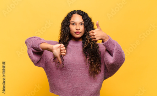 young hispanic woman feeling confused, clueless and unsure, weighting the good and bad in different options or choices