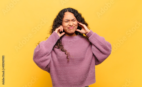 young hispanic woman looking angry, stressed and annoyed, covering both ears to a deafening noise, sound or loud music photo