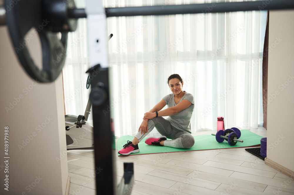 Young athletic woman sitting on the exercising mat and looking at the camera. Young athletic woman sitting on the exercising mat and looking at the camera.