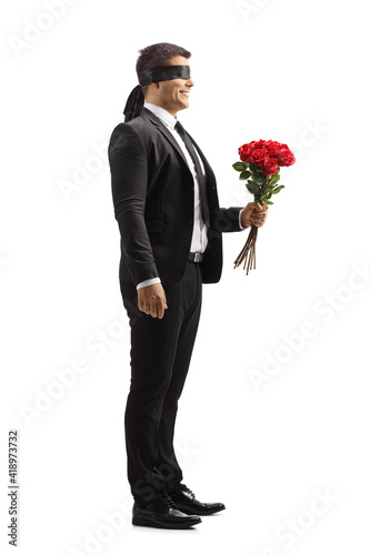 Full length profile shot of a man in a suit with blindfold holding a bunch of red roses