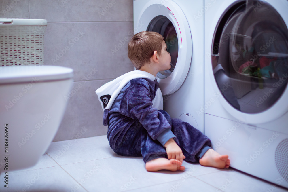 the toddler is looking into the washing machine while wash the toddler is looking into the washing machine while wash