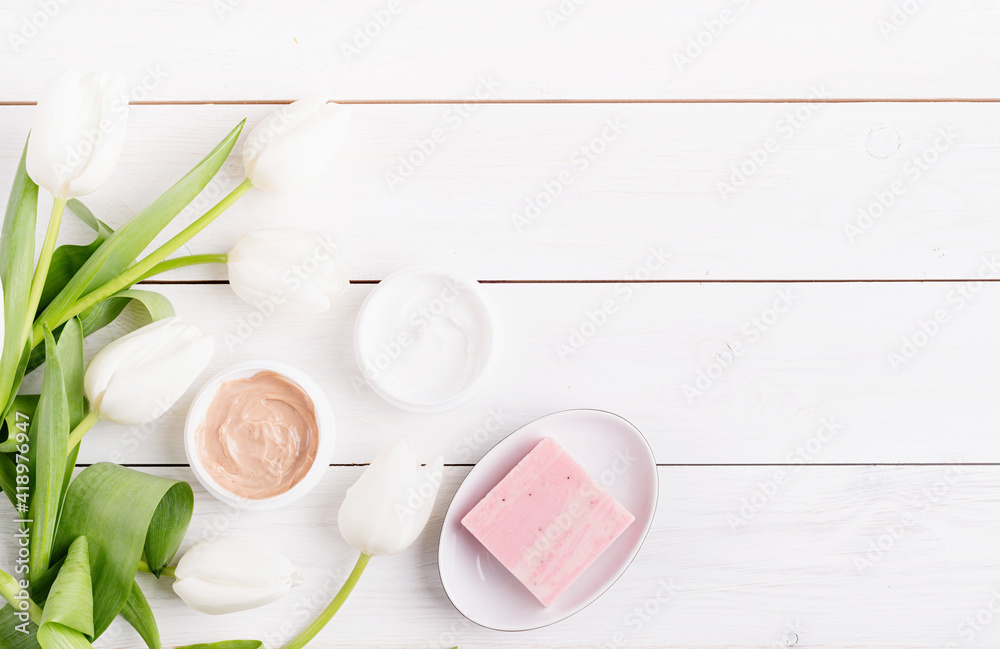 Top view of cosmetic creams and soap with white tulips top view flat lay on white wooden background Top view of cosmetic creams and soap with white tulips top view flat lay on white wooden background