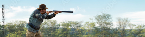 A hunter with a gun in his hands in hunting clothes in the autumn forest in search of a trophy. A man stands with weapons and hunting dogs tracking down the game.