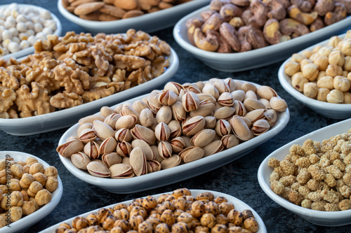 Pistachios in selective focus. Nuts on plate on a dark background. Walnut, Chickpeas, White Chickpeas, Dry mulberry, almond, cashew, pistachio. Types of nuts on the plate.
