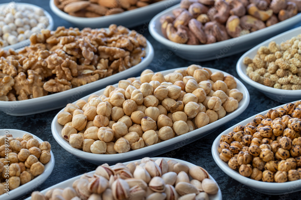 Hazelnuts in selective focus. Nuts on plate on a dark background. Walnut, Chickpeas, White Chickpeas, Dry mulberry, almond, cashew, pistachio. Types of nuts on the plate. Hazelnuts in selective focus. Nuts on plate on a dark background. Walnut, Chickpeas, White Chickpeas, Dry mulberry, almond, cashew, pistachio. Types of nuts on the plate.