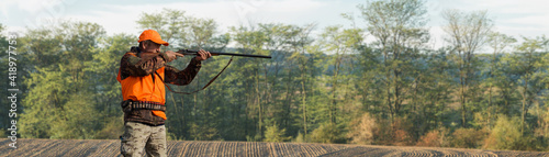 A hunter with a gun in his hands in hunting clothes in the autumn forest in search of a trophy. A man stands with weapons and hunting dogs tracking down the game.