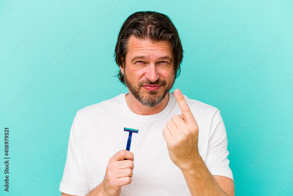 Middle age dutch man holding a razor blade isolated on blue background pointing with finger at you as if inviting come closer. Middle age dutch man holding a razor blade isolated on blue background pointing with finger at you as if inviting come closer.