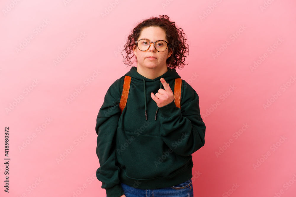 Young student woman with Down syndrome isolated on pink background pointing with finger at you as if inviting come closer. Young student woman with Down syndrome isolated on pink background pointing with finger at you as if inviting come closer.