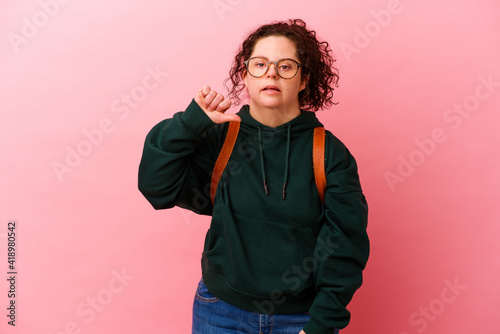 Young student woman with Down syndrome isolated on pink background showing a dislike gesture, thumbs down. Disagreement concept.