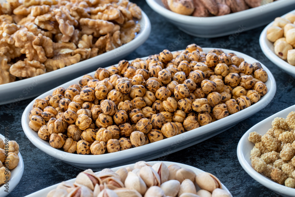 Roasted chickpeas in selective focus. Nuts on plate on a dark background. Walnut, Chickpeas, White Chickpeas, Dry mulberry, almond, cashew, pistachio. Types of nuts on the plate. Roasted chickpeas in selective focus. Nuts on plate on a dark background. Walnut, Chickpeas, White Chickpeas, Dry mulberry, almond, cashew, pistachio. Types of nuts on the plate.