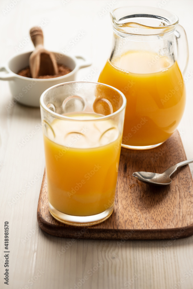 Top view of glass and jug with orange juice, spoon, and brown sugar, on white wood, in vertical Top view of glass and jug with orange juice, spoon, and brown sugar, on white wood, in vertical