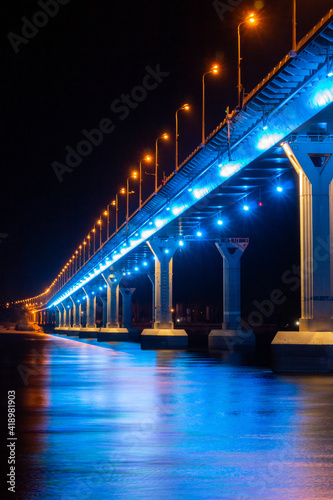 Side view of colourful bridge illuminated with blue color lights at the night. Bridge stands on Volga river in Russia. Blue light is reflected in the water.