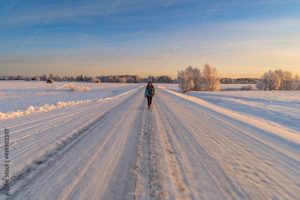 A beautiful woman wearing colourful cloth walking on the empty road with snow covered landscape