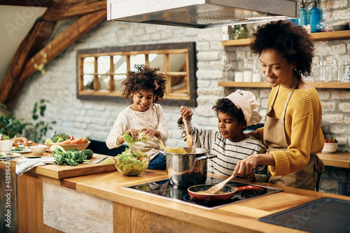 Happy black mother and her kids preparing food in the kitchen.