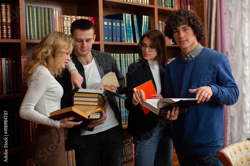 a group of students stand together in the library reading books and discussing a team project. Photos for educational sites  college advertising  schools. High quality photo