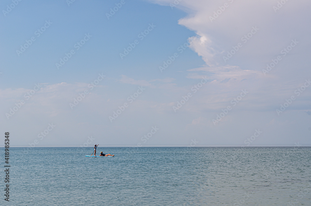 Propelling oneself through the water with a paddle. Child stand up paddle boarding on a calm sea. Little girl rides a board, pastime with her grandfather - awesome active recreation during vacation. Propelling oneself through the water with a paddle. Child stand up paddle boarding on a calm sea. Little girl rides a board, pastime with her grandfather - awesome active recreation during vacation.