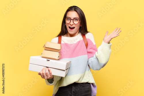 young pretty woman feeling happy, excited, surprised or shocked, smiling and astonished at something unbelievable. take aeay fast food concept photo