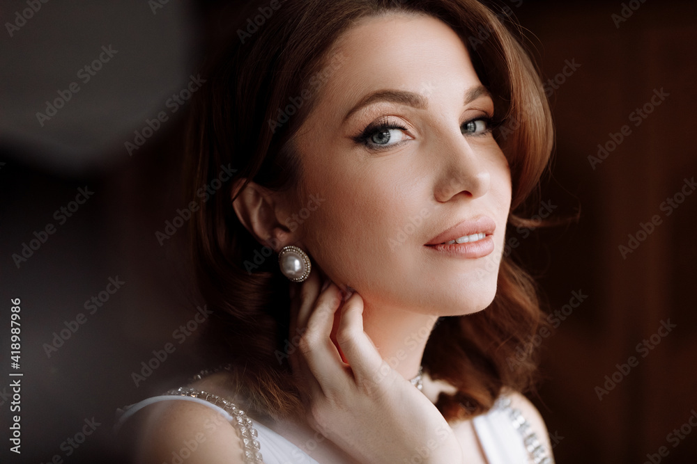 beauty concept. portrait of a beautiful young showy brunette woman with bright pin-up make-up and hairstyle. girl in luxury dress and earrings pearls and looking in camera. international women's day