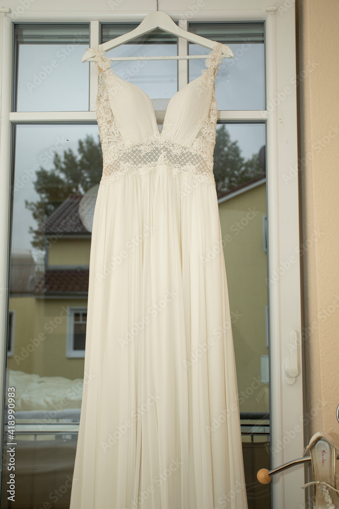 Getting Ready, weißes Brautkleid hängt am Fenster, , Im Fenster spiegeln sich die Bäumer. Getting Ready, weißes Brautkleid hängt am Fenster, , Im Fenster spiegeln sich die Bäumer.