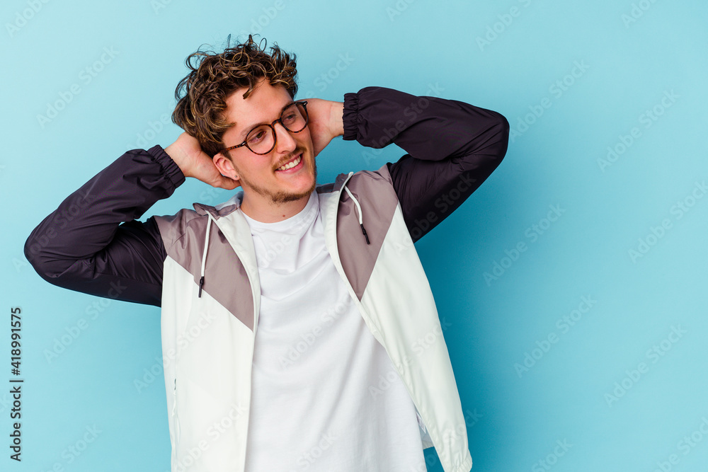 Young caucasian man wearing eyeglasses isolated on blue background feeling confident, with hands behind the head. Young caucasian man wearing eyeglasses isolated on blue background feeling confident, with hands behind the head.