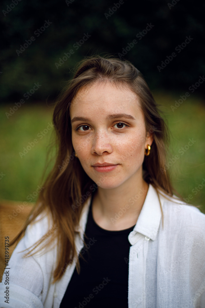 portrait of a young woman without makeup in a white shirt and black t-shirt in a park or garden with a blurred background bokeh effect