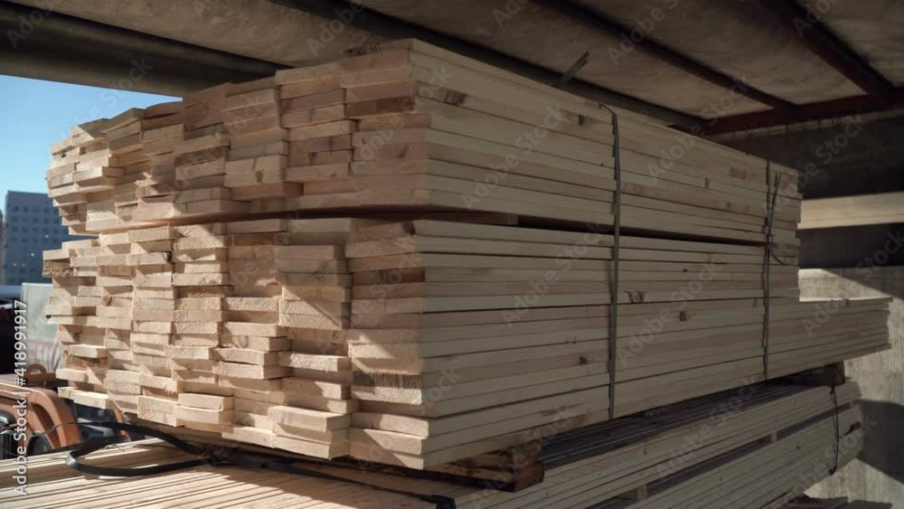 A forklift is loading wood planks into the truck. Transportation of wooden beams. Building materials for a house made of wood. Roof rafter system. Natural forestry planed products. Unloading pack.