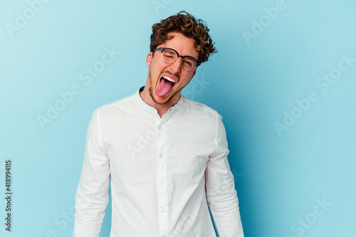 Young caucasian business man isolated on blue background funny and friendly sticking out tongue.