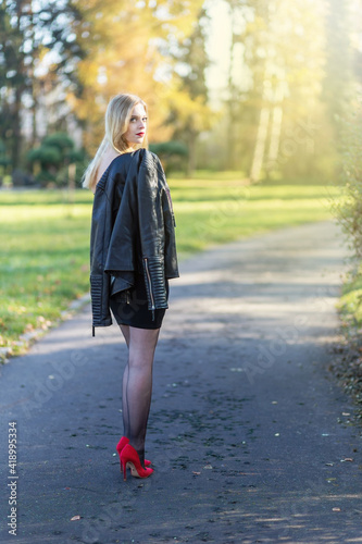 Attractive long hair girl dressed in leather jacket is  turning back to camera in autumn park. Vertically.  © frank11