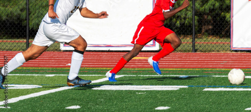 Soccer player in red uniform dribbling the ball with player in white uniform chasing