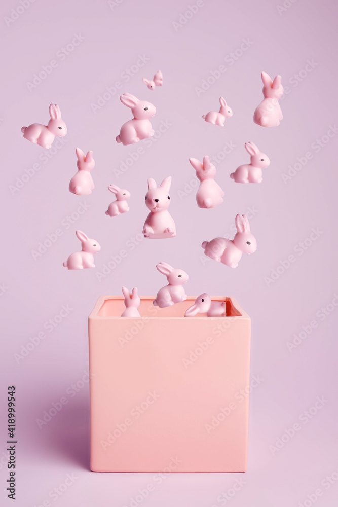 Creative layout with bunch of pink bunnies and rabbits flying out of box on pastel pink background. Minimal Easter holiday concept. Contemporary spring holiday animal layout.