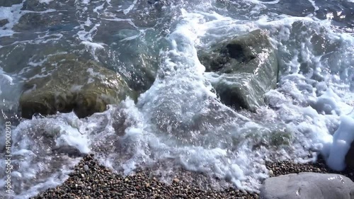 Sea waves wash the stones and pebble shore of the summer coast. Summer coast of the Black Sea. Slow motion video from 100 to 25 fps, no audio