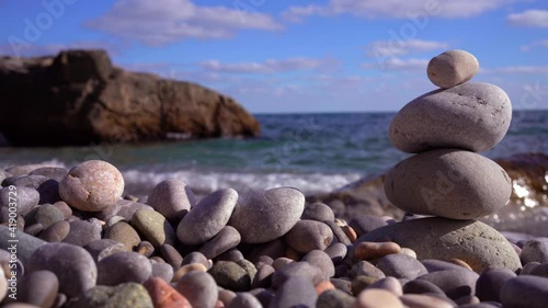 A pyramid of four pebble stones stands on the shore of a summer seaside resort. Waves one after another roll to the shore