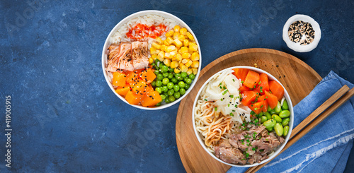 Banner, Two poke bowls, flamed salmon, pulled pork, vegetables, rice, sauces. Top view, close-up. Hawaiian dish, blue dark background. Trendy asian food. Healthy and clean eating concept.