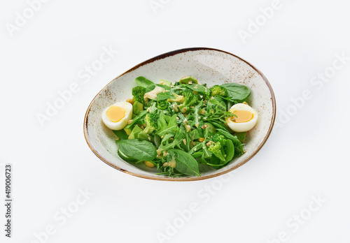 Tasty green healthy salad with spinach leaves, avocado and boiled eggs in bowl on white background