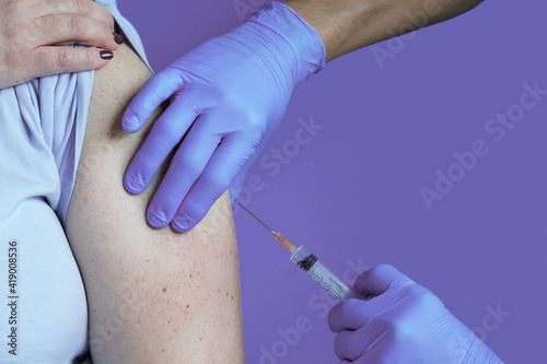 Doctor holding syringe making covid 19 vaccination injection dose in shoulder of female patient.