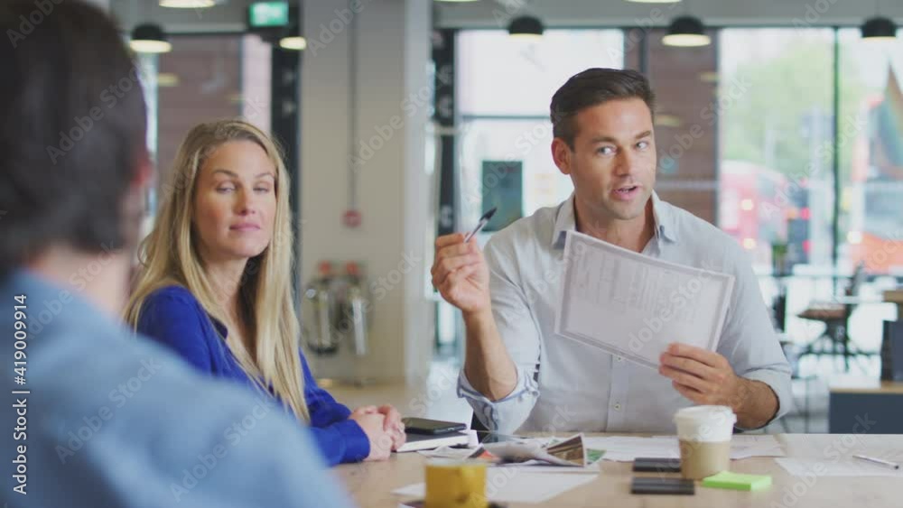 Business team sitting around table in office discussing document together - shot in slow motion Business team sitting around table in office discussing document together - shot in slow motion