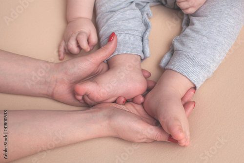 Mother holds the legs of her baby in her hands. Close-up. Photo session for one year. Textile beige background.