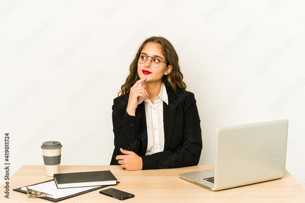 Young caucasian business woman working on her desktop isolated looking sideways with doubtful and skeptical expression. Young caucasian business woman working on her desktop isolated looking sideways with doubtful and skeptical expression.