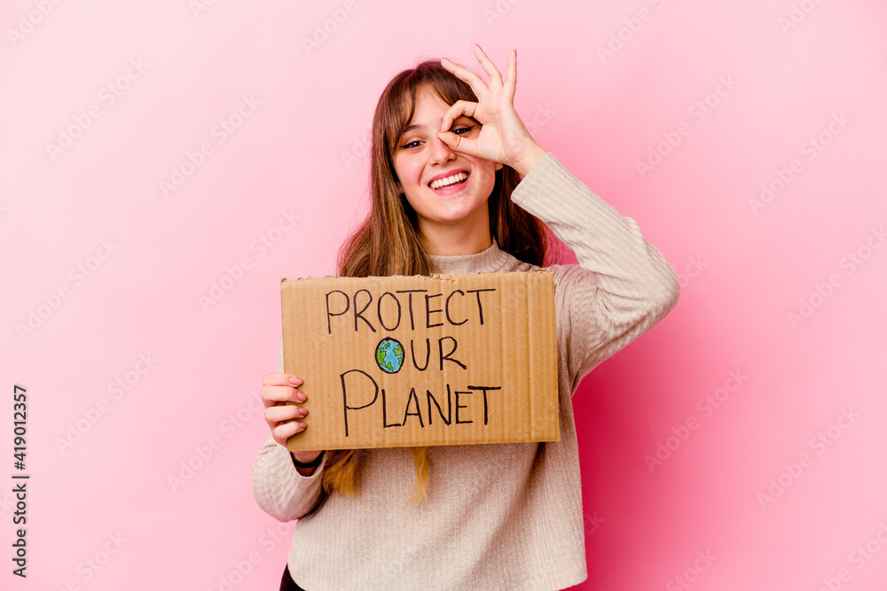 Young caucasian woman holding a Protect our planet placard isolated excited keeping ok gesture on eye.