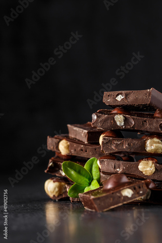 Stack of chocolate slices with mint leaf.Hazelnut and almond milk and dark chocolate pieces tower.Sweet food photo concept. The chunks of broken chocolate