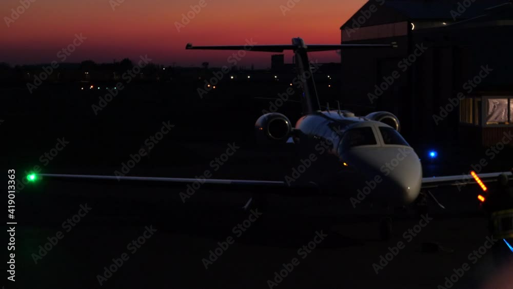 Small Private Jet Being Guided by Marshaller to Parking Spot. Night.
