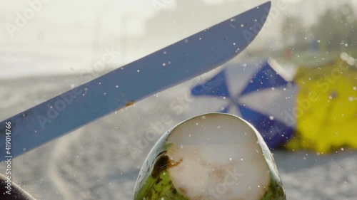 Close-up of opening coconut with machete at beach, slow motion. photo