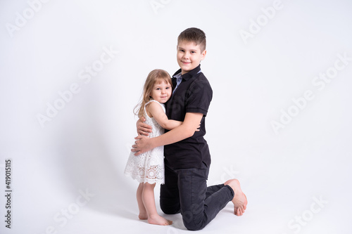 handsome older brother teenager hugging his cute little sister on white background