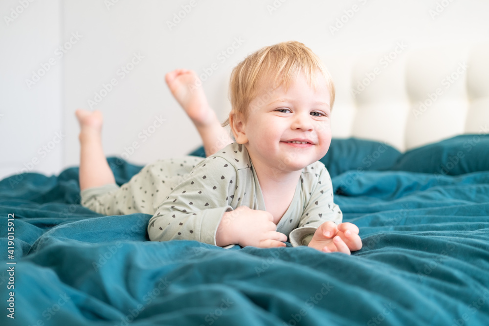 Little healthy toddler boy in green pajamas having fun lying in bed at home Little healthy toddler boy in green pajamas having fun lying in bed at home
