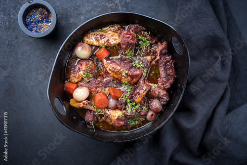 Modern style traditional French coq au vin with vegetable marinated in Burgundy sauce as top view in a design casserole