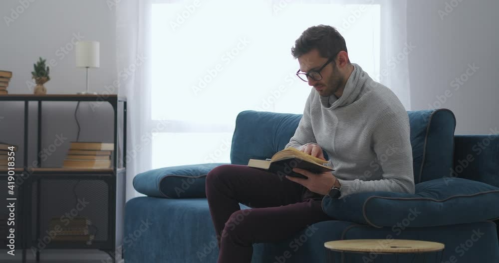 intelligent man with glasses is reading book sitting at apartment at weekend, isolation and lockdown intelligent man with glasses is reading book sitting at apartment at weekend, isolation and lockdown